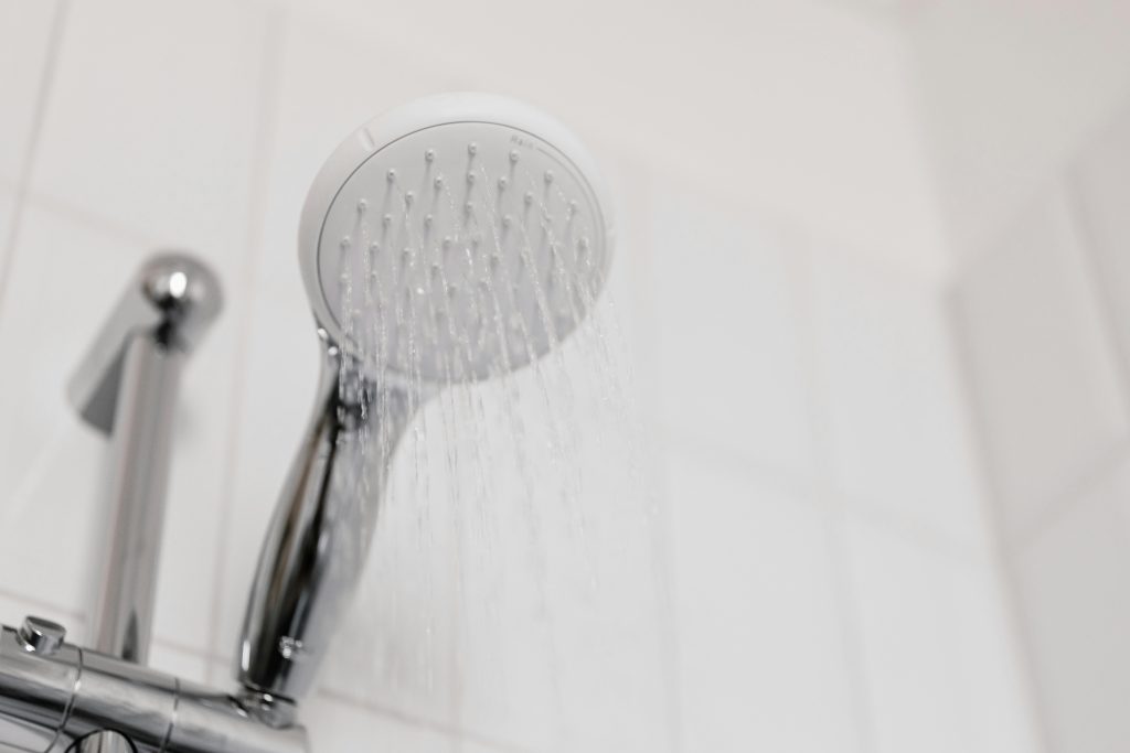 Stylish clean shower head with water flow in a white tiled bathroom.